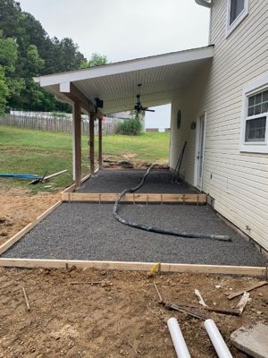 Wood forms and compacted gravel base set beside a house, ready for a concrete pour