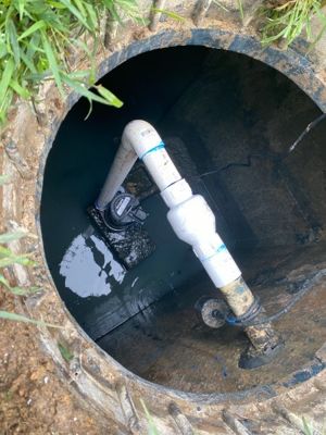 View down into a septic pump tank showing the pump and new PVC discharge plumbing