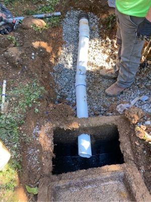 Open septic tank with a new PVC line bedded in gravel next to a brick house