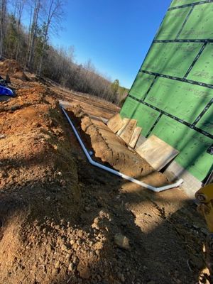 White PVC sewer line laid in a freshly dug trench beside a new-construction house